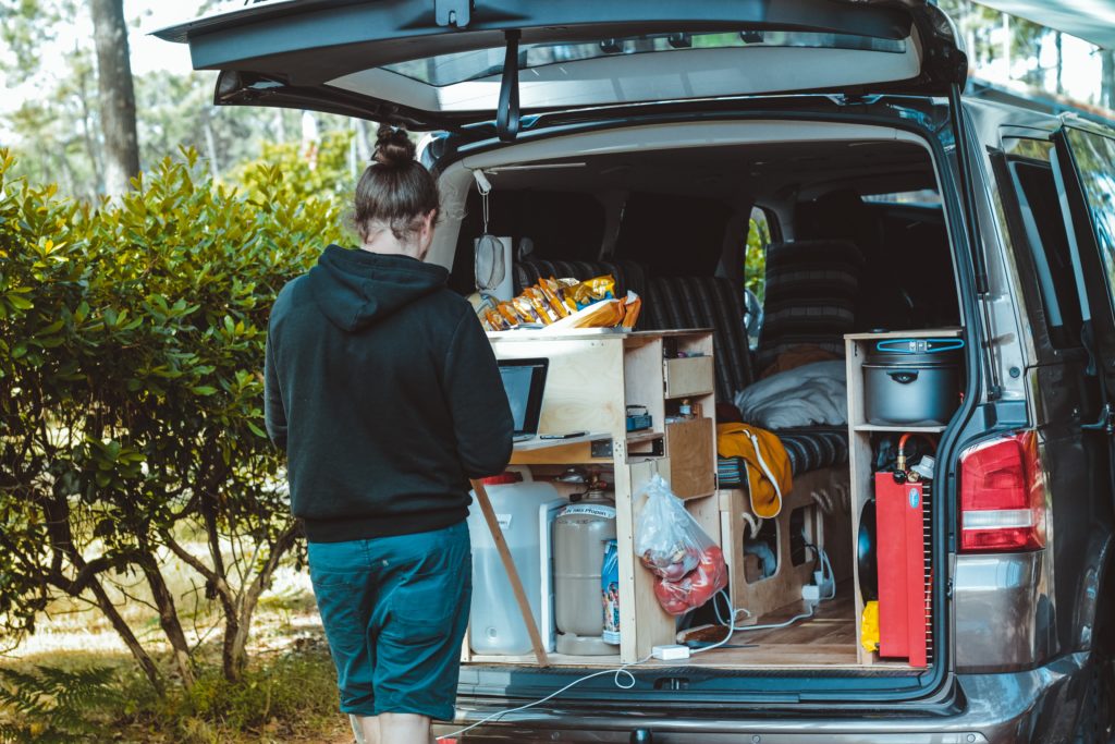 Person working on a laptop at a stand up desk coming out the back of a camper van. Photo by Brina Blum on Unsplash